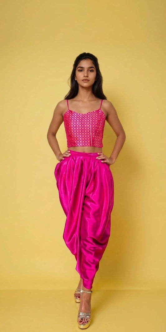 A young girl modeling a bright pink two-piece outfit consisting of a sleeveless, embellished crop top and matching draped pants, set against a solid yellow background.